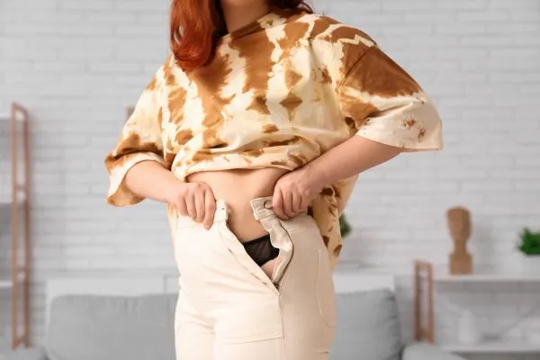 Image of woman trying to do her trousers up after pregnancy weight gain Tewkesbury