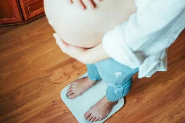 Image of woman weighing herself and experiencing weight gain through pregnancy Tewkesbury